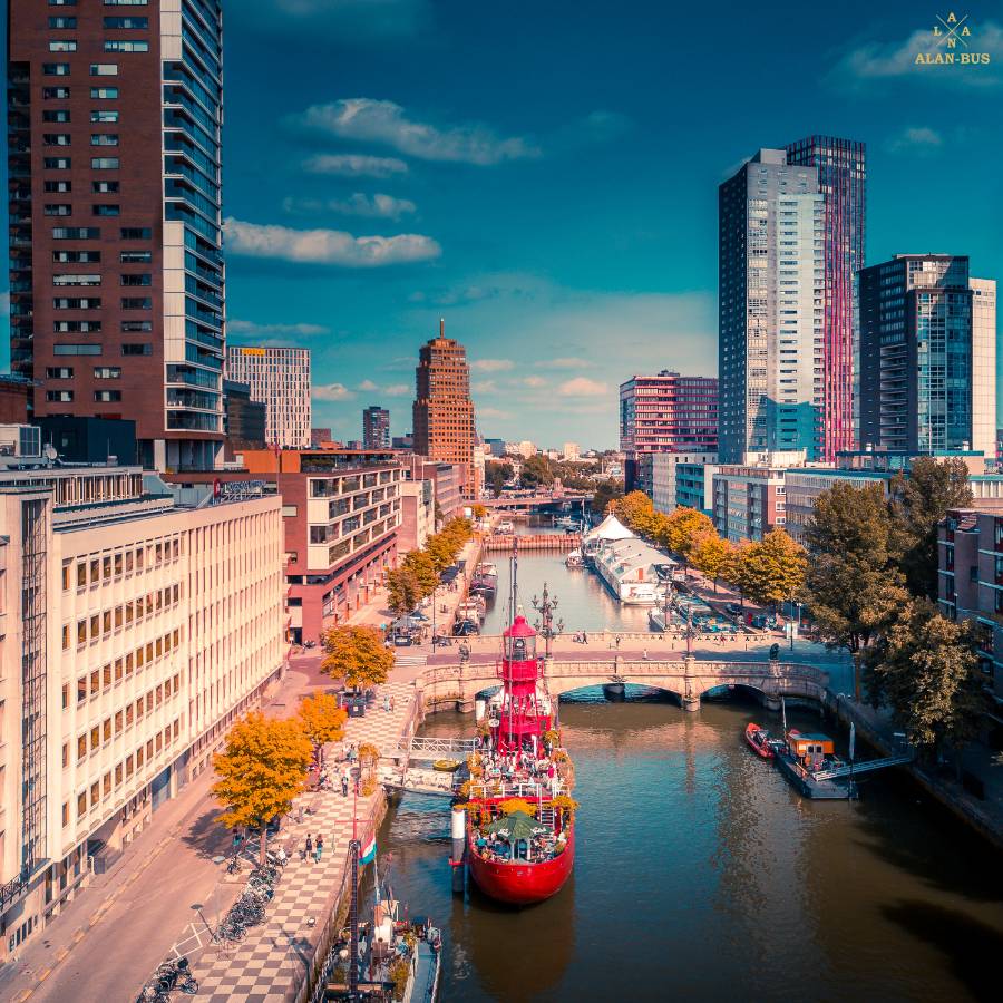 Panorama nowoczesnej dzielnicy Rotterdamu z kanałem, czerwonym statkiem i wysokimi wieżowcami w tle pod błękitnym niebem